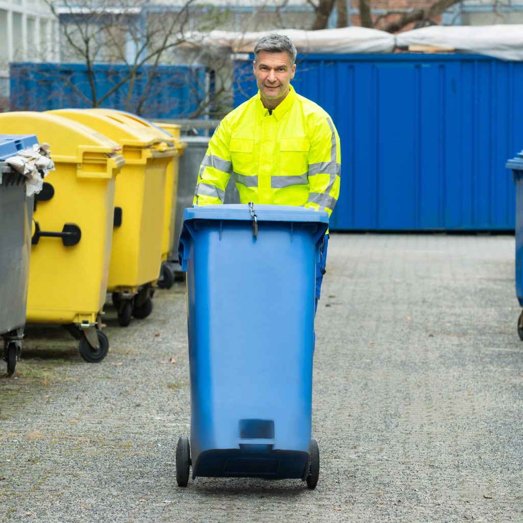 Happy Male Worker Walking With Dustbin On Street During Day